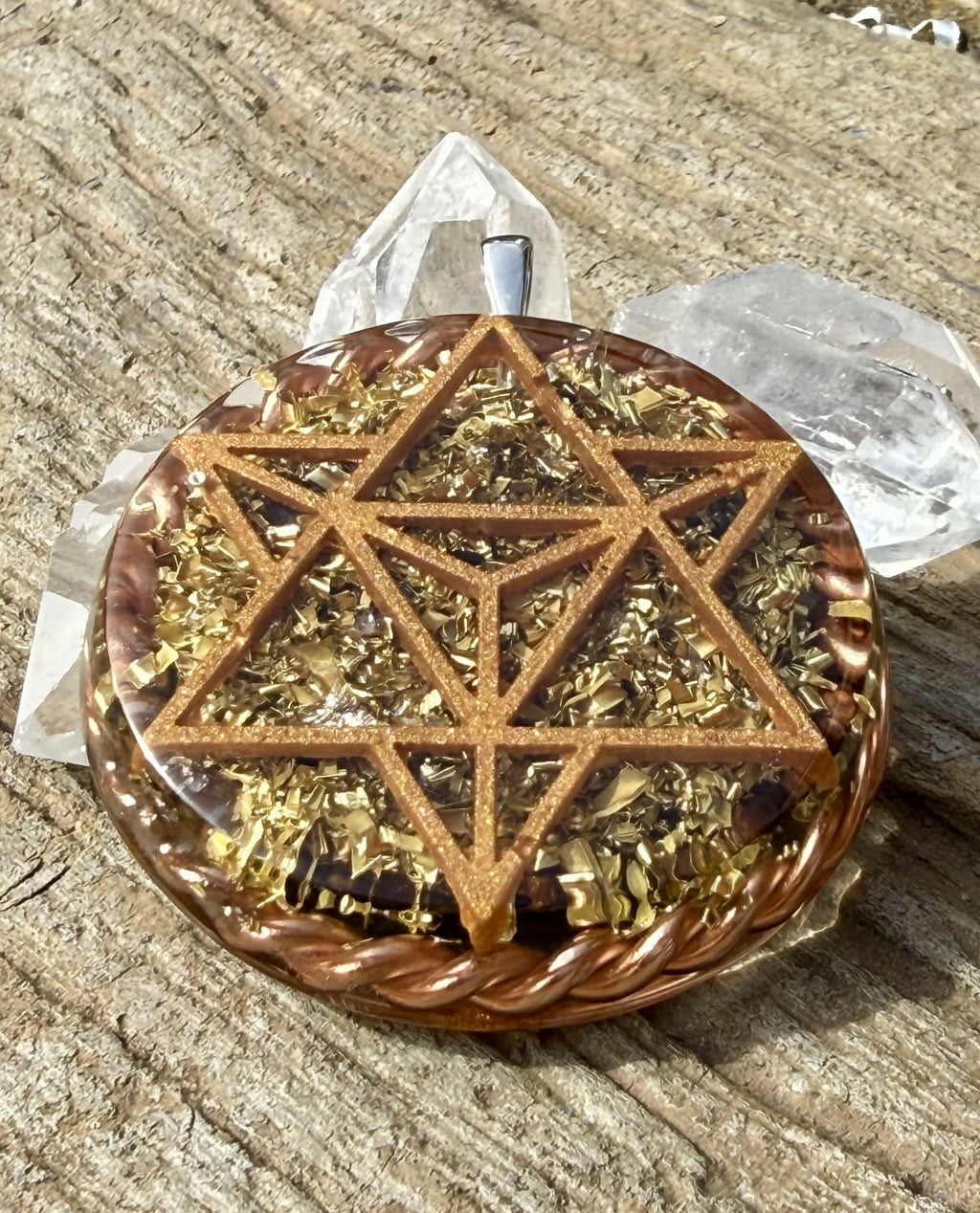 Front view of the copper-coloured star tetrahedron design over gold-coloured flakes and dark stones