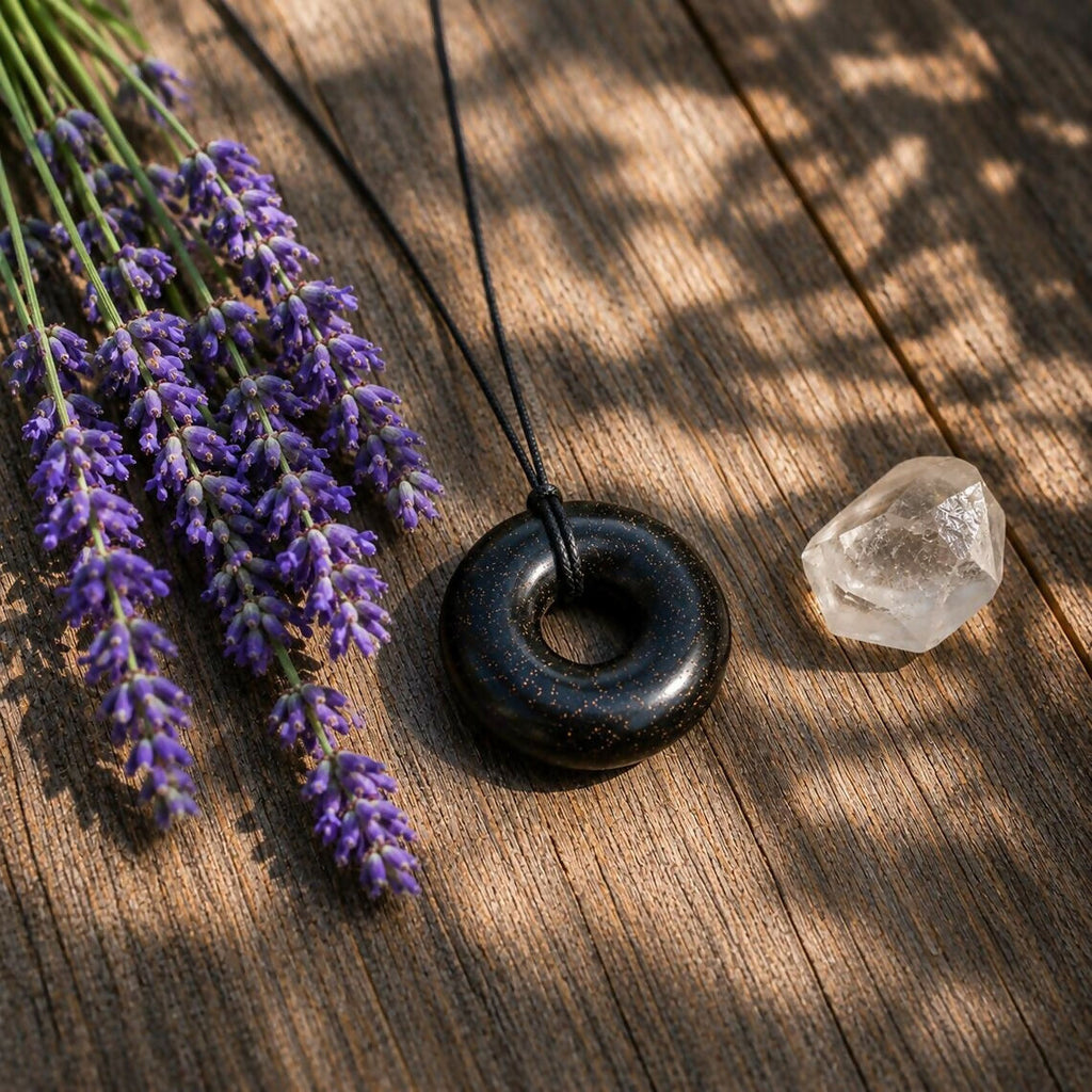 The black donut pendant on a wooden surface beside lavender sprigs and a clear quartz crystal