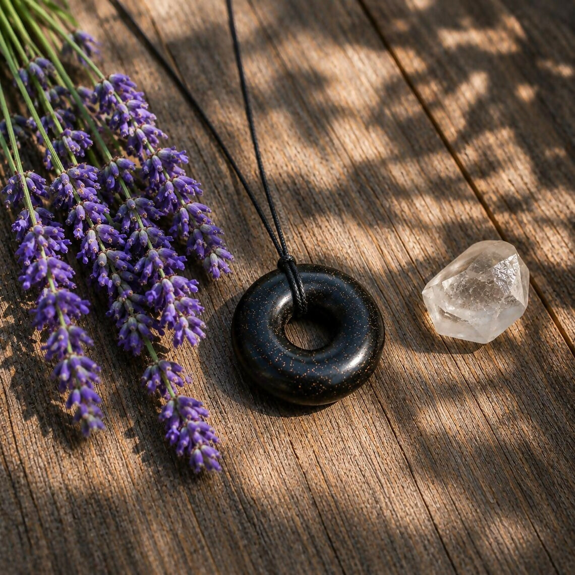 The black donut pendant on a wooden surface beside lavender sprigs and a clear quartz crystal
