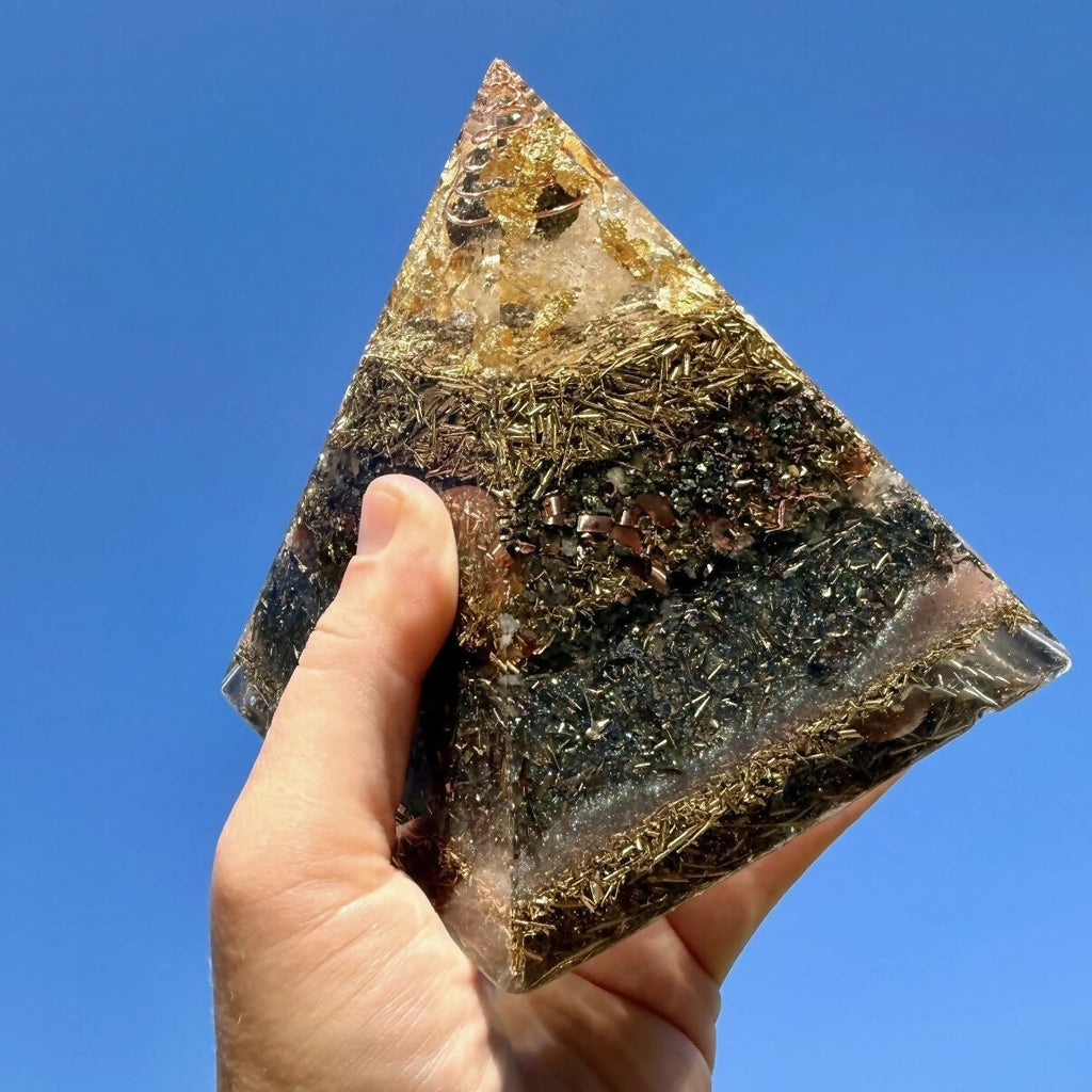 Pyramid held up against a blue sky, showing its golden apex and dark metal-shaving layers
