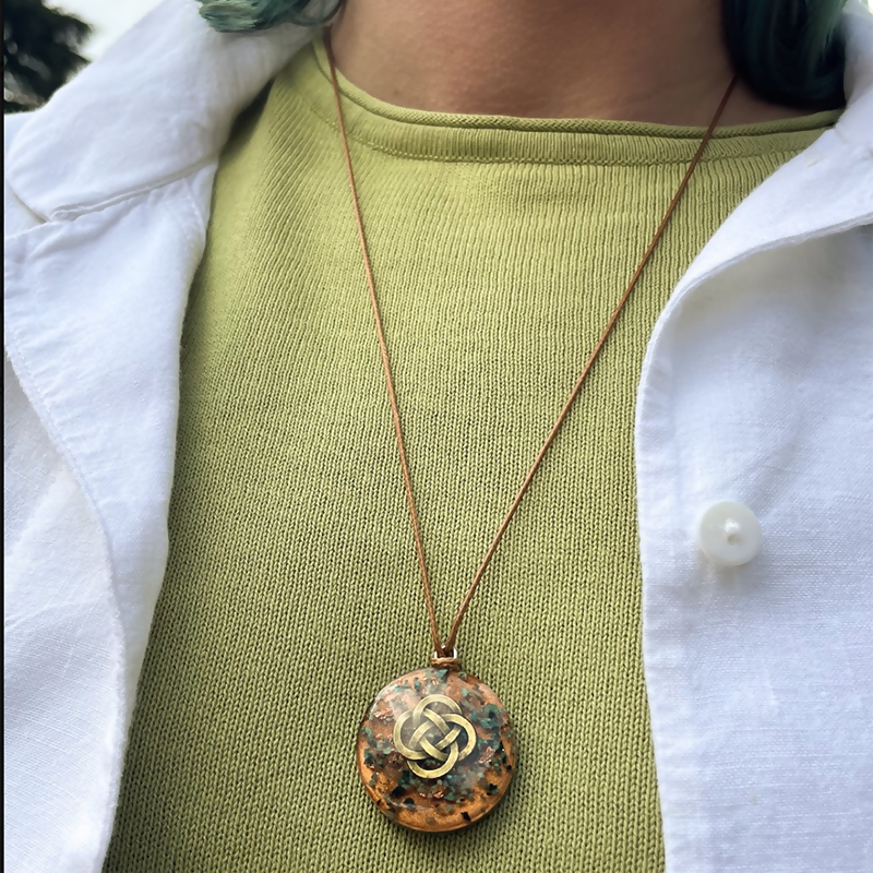 Pendant worn on a long brown cord over a green top and white shirt